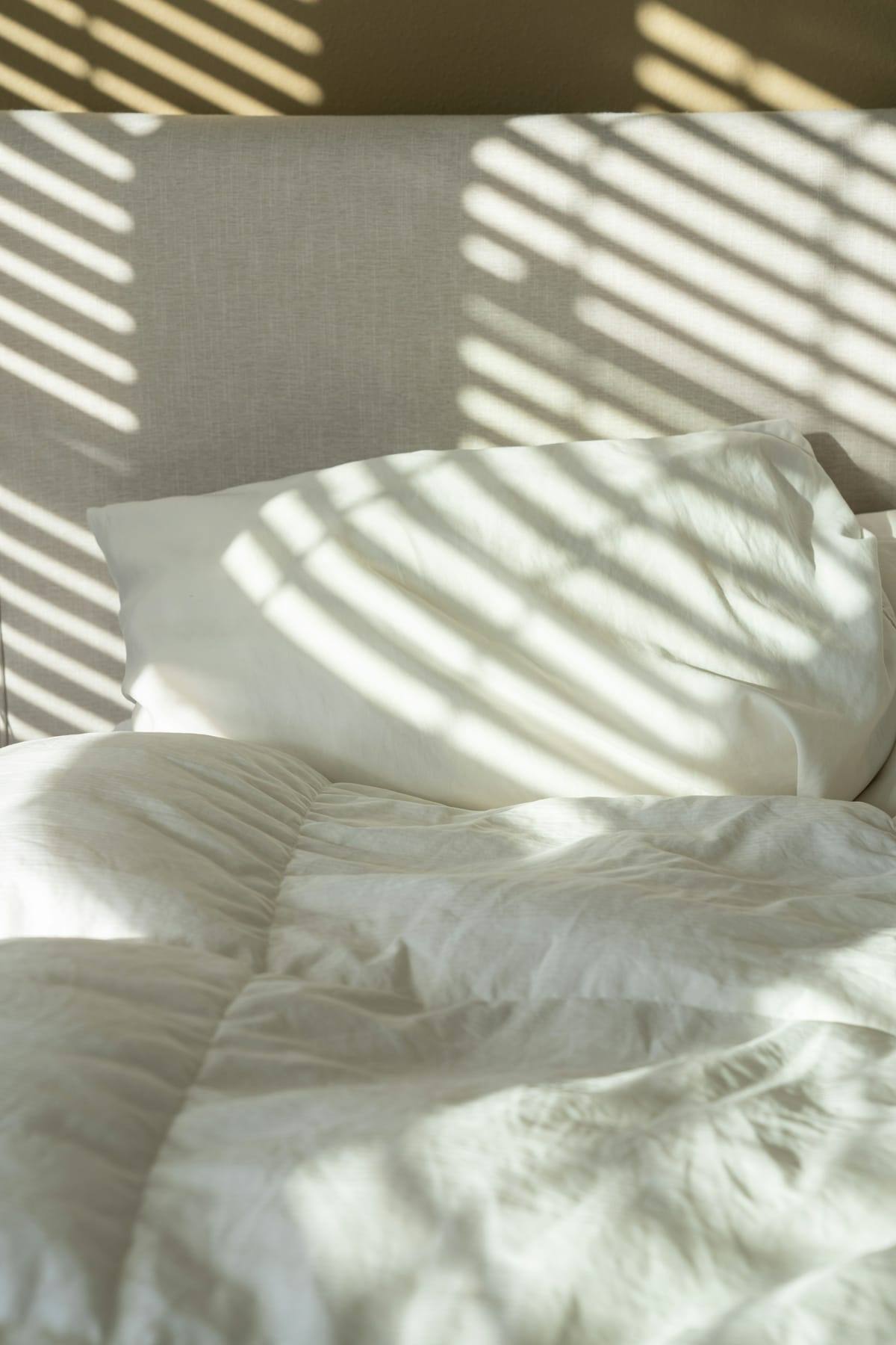 Freshly made bed with white linen in morning light