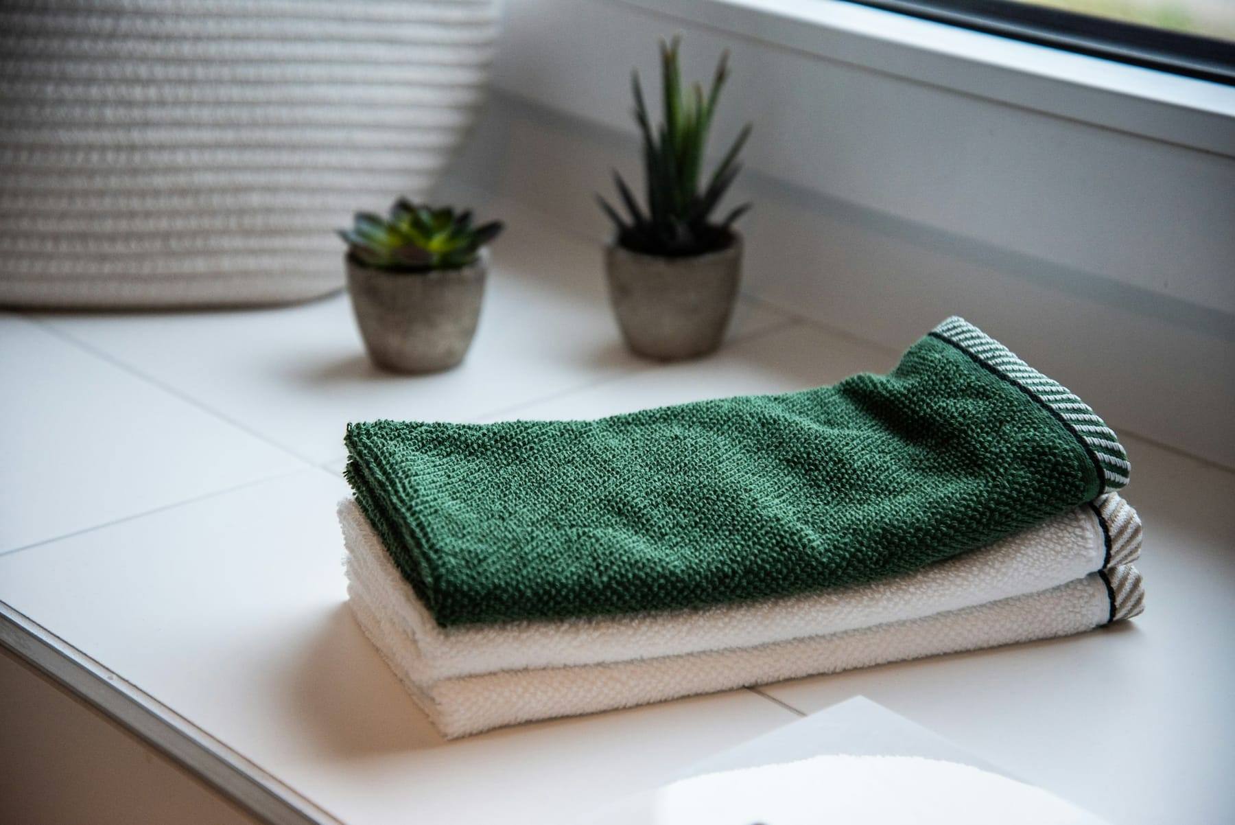 Neatly folded green towels beside small potted plants